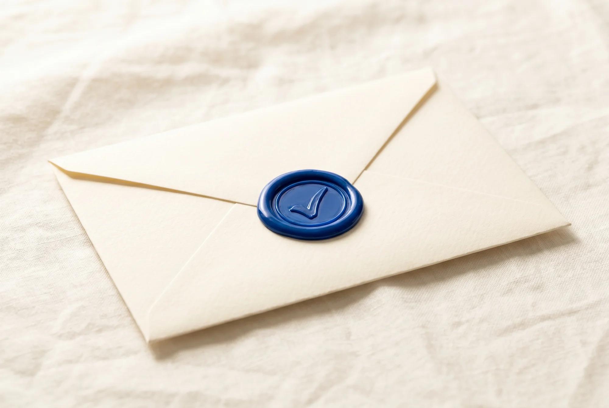 A cream envelope closed with a blue wax seal on white linen